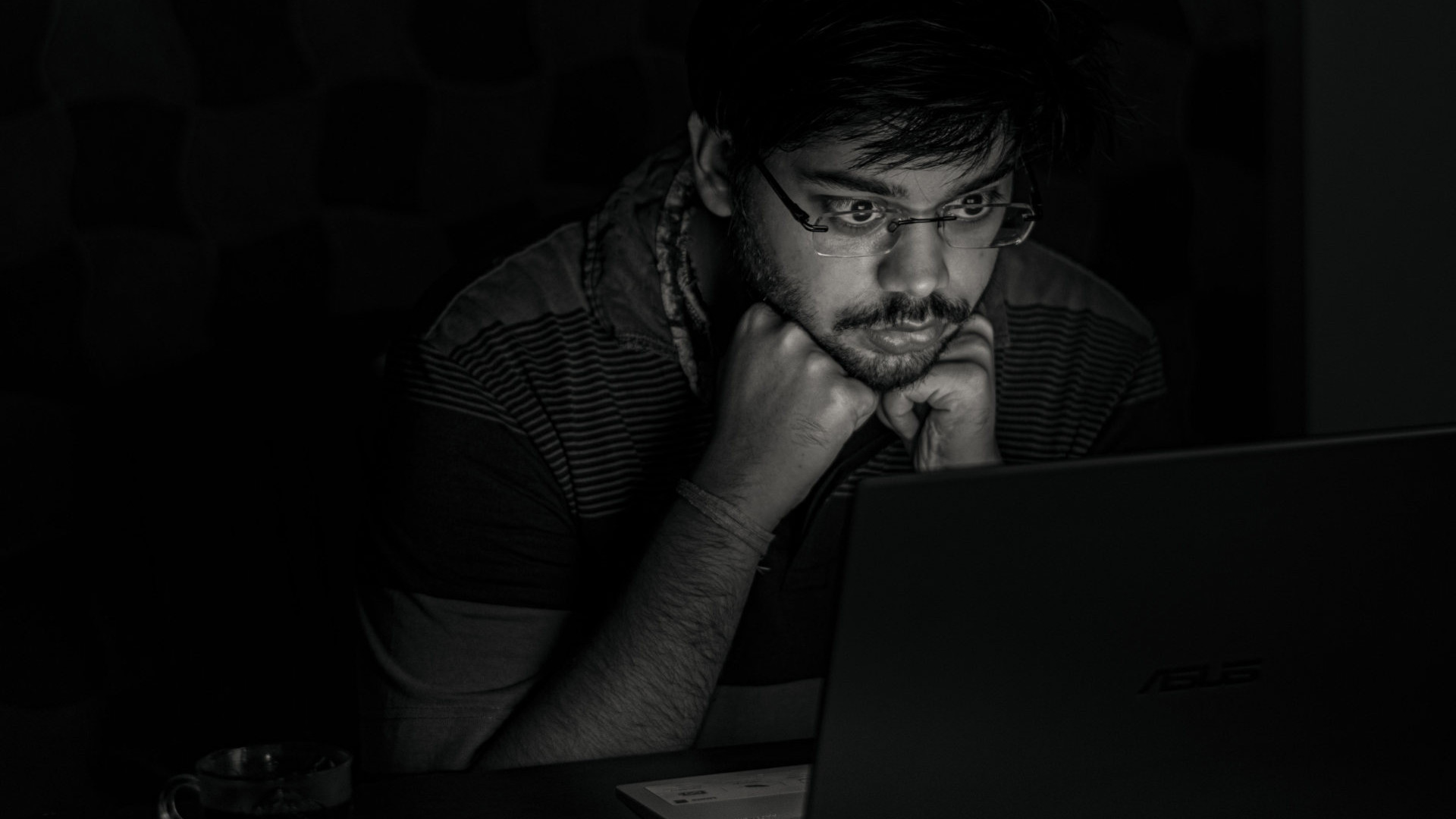 Man staart 's avonds peinzend naar zijn laptopscherm, handen onder z'n kin